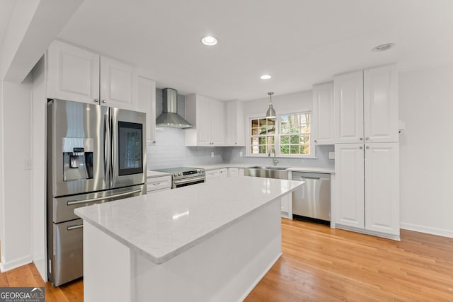 kitchen featuring wall chimney range hood, stainless steel appliances, a sink, white cabinets, and a kitchen island