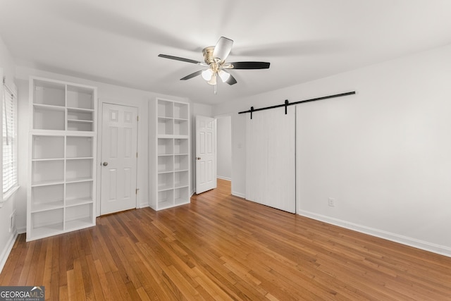 unfurnished bedroom featuring baseboards, a ceiling fan, wood finished floors, and a barn door