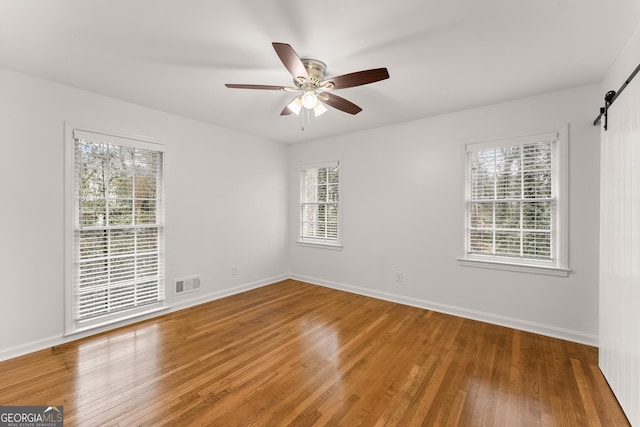 unfurnished room featuring wood finished floors, baseboards, visible vents, a barn door, and ceiling fan