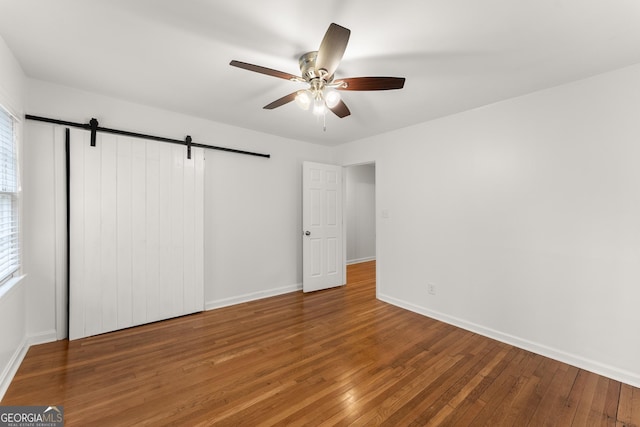 unfurnished bedroom with baseboards, wood finished floors, multiple windows, and a barn door