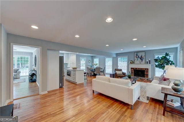 living room featuring light wood-style flooring, baseboards, a brick fireplace, and recessed lighting