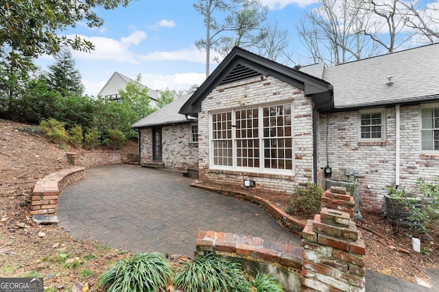 rear view of house featuring brick siding, a patio, and roof with shingles