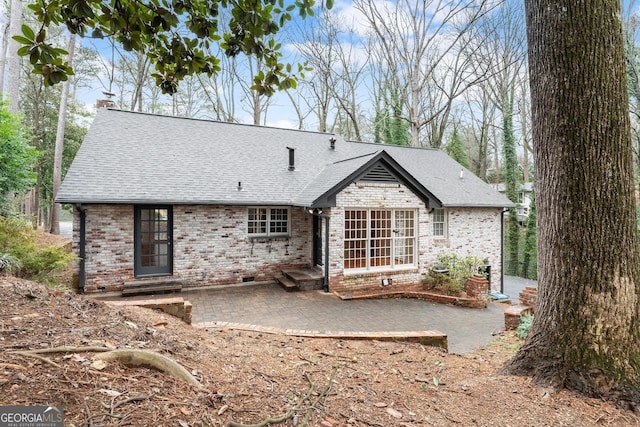 rear view of property featuring a patio, a chimney, a shingled roof, and brick siding