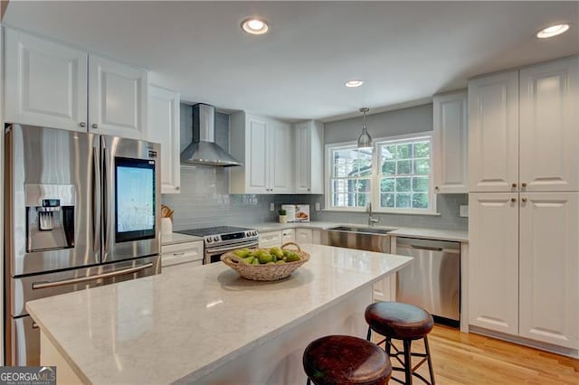 kitchen featuring a kitchen island, white cabinetry, a sink, wall chimney exhaust hood, and stainless steel appliances