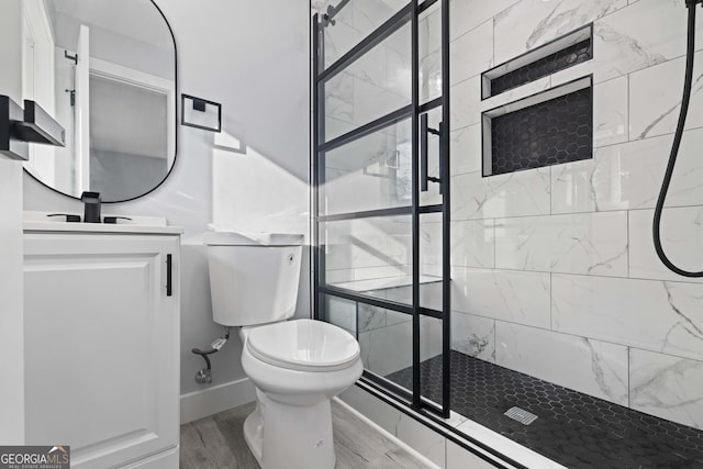 bathroom with hardwood / wood-style floors, toilet, vanity, and a tile shower