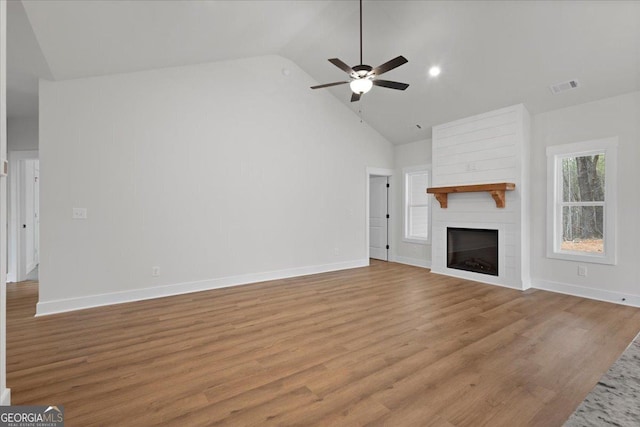 unfurnished living room with ceiling fan, a large fireplace, high vaulted ceiling, and light hardwood / wood-style flooring