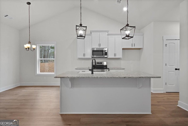 kitchen with light stone counters, white cabinetry, stainless steel appliances, and a center island with sink