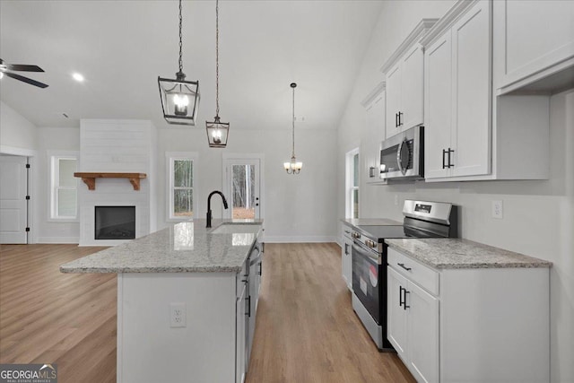 kitchen with sink, appliances with stainless steel finishes, white cabinetry, hanging light fixtures, and an island with sink