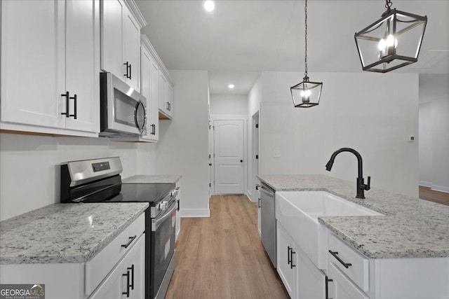 kitchen with hanging light fixtures, appliances with stainless steel finishes, a center island with sink, and white cabinets