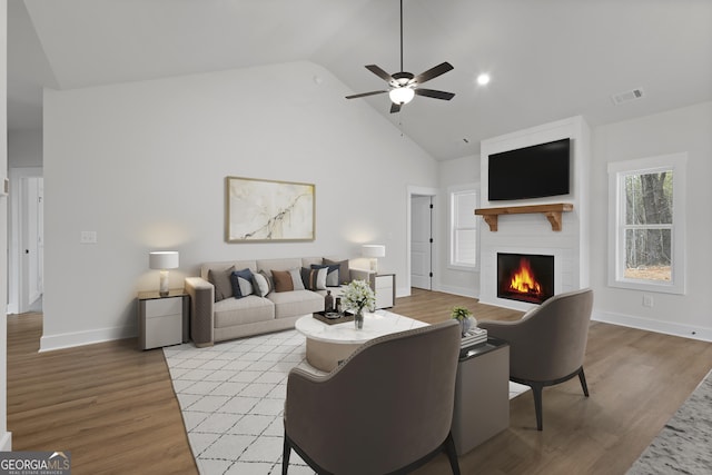 living room with ceiling fan, a large fireplace, high vaulted ceiling, and light hardwood / wood-style floors