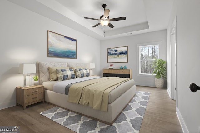 bedroom featuring ceiling fan, a raised ceiling, and light hardwood / wood-style floors