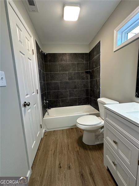 full bathroom with wood-type flooring, toilet, vanity, and tiled shower / bath combo