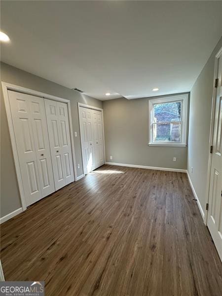 unfurnished bedroom featuring dark hardwood / wood-style floors and two closets