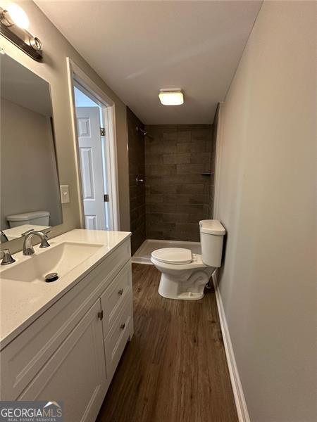 bathroom with a tile shower, hardwood / wood-style floors, toilet, and vanity