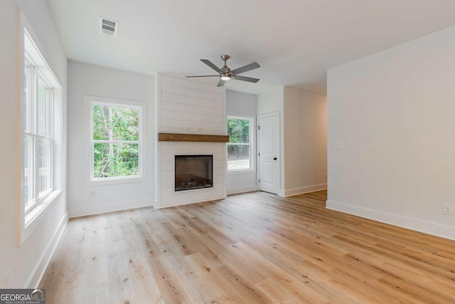 unfurnished living room with a fireplace, light wood-type flooring, ceiling fan, and plenty of natural light