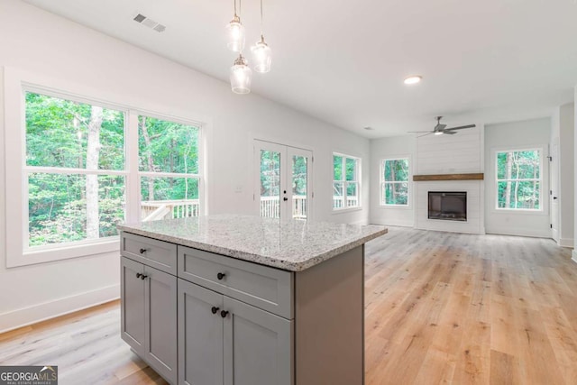 kitchen featuring decorative light fixtures, gray cabinets, light hardwood / wood-style floors, and light stone countertops