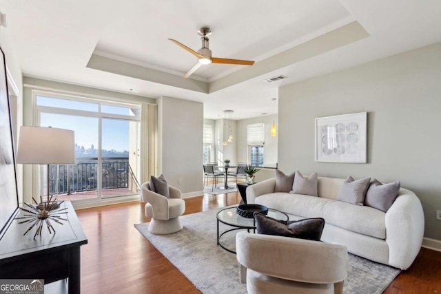 living room featuring ceiling fan, wood-type flooring, and a tray ceiling