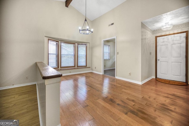 entryway with wood-type flooring, a chandelier, beam ceiling, and high vaulted ceiling