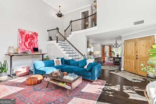 living room featuring wood-type flooring, a high ceiling, a notable chandelier, and ornamental molding