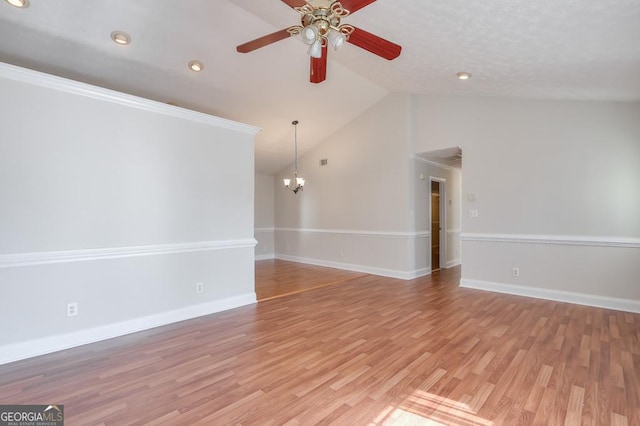 empty room featuring vaulted ceiling, ceiling fan with notable chandelier, and light wood-type flooring