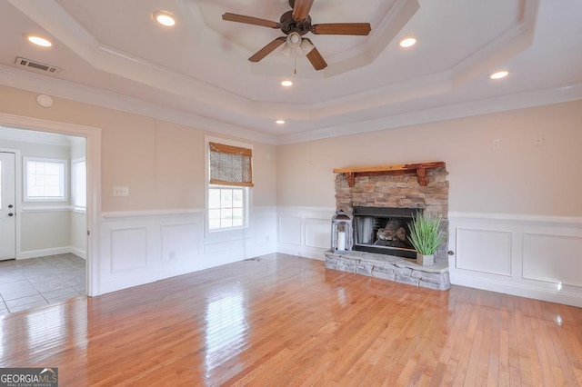 unfurnished living room featuring a tray ceiling, a wealth of natural light, light hardwood / wood-style floors, and a stone fireplace