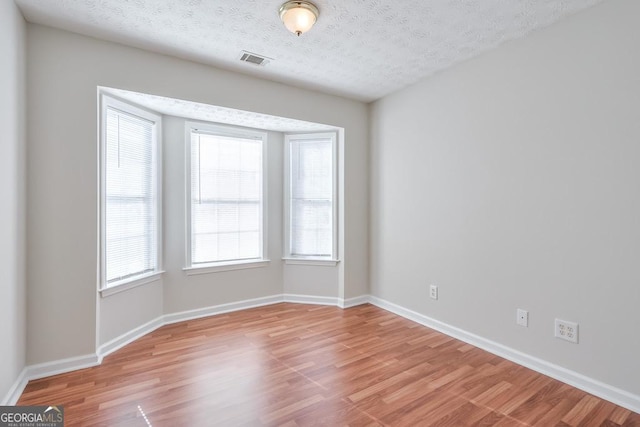 spare room featuring a textured ceiling and light hardwood / wood-style floors