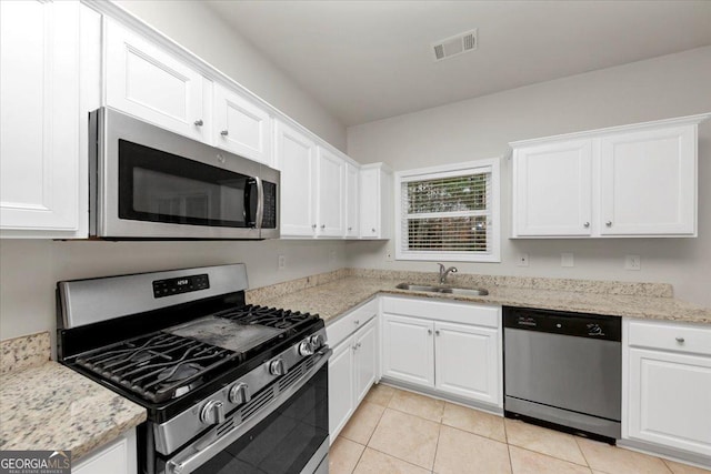 kitchen with sink, white cabinetry, light tile patterned floors, light stone counters, and stainless steel appliances