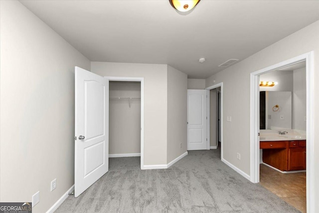 unfurnished bedroom with a closet, light carpet, and ensuite bath