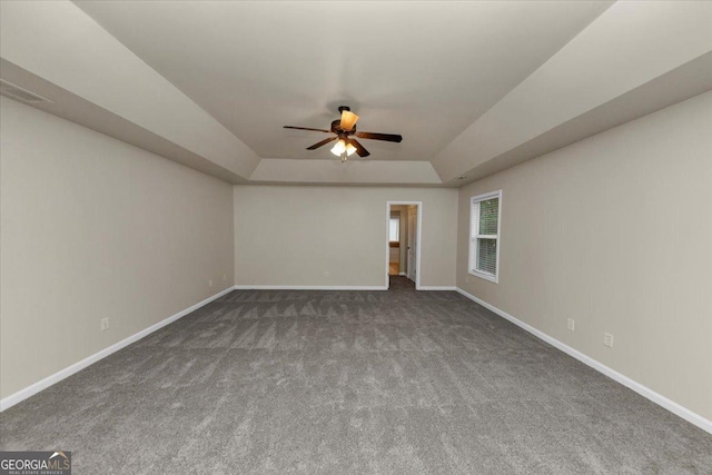 unfurnished room with ceiling fan, dark carpet, and a tray ceiling