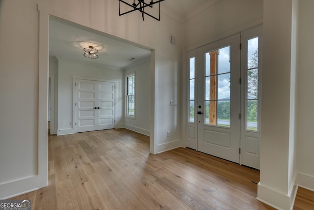 foyer entrance featuring crown molding, light wood finished floors, baseboards, and an inviting chandelier