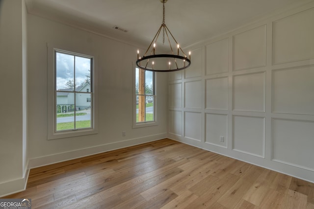 unfurnished dining area featuring an inviting chandelier, a decorative wall, light wood-type flooring, and visible vents