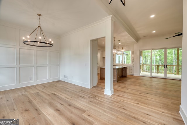 unfurnished dining area with ornamental molding, a decorative wall, light wood-type flooring, and a notable chandelier