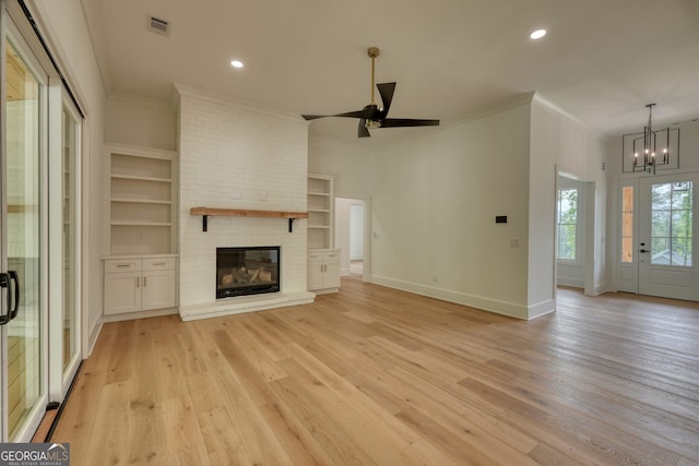 unfurnished living room with crown molding, light wood finished floors, a brick fireplace, ceiling fan with notable chandelier, and baseboards
