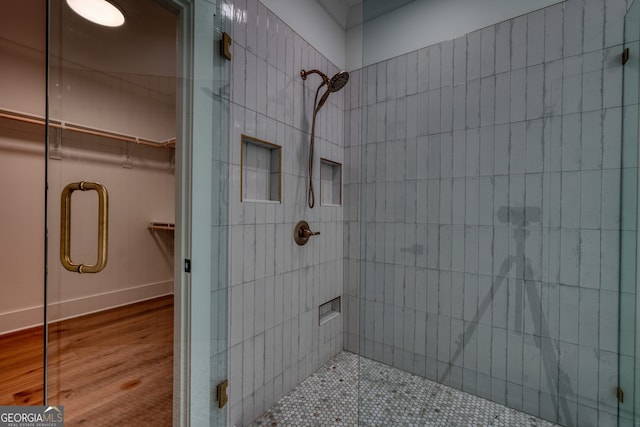 full bath featuring baseboards, a spacious closet, a shower stall, and wood finished floors