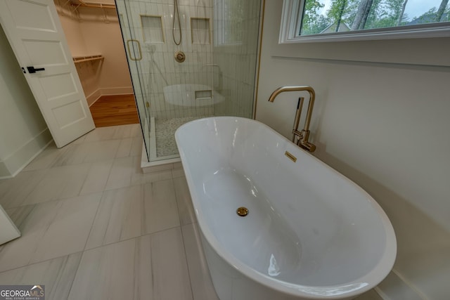 full bath with tile patterned flooring, a freestanding tub, baseboards, a walk in closet, and a shower stall