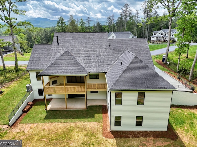 back of property with a patio, roof with shingles, and a yard