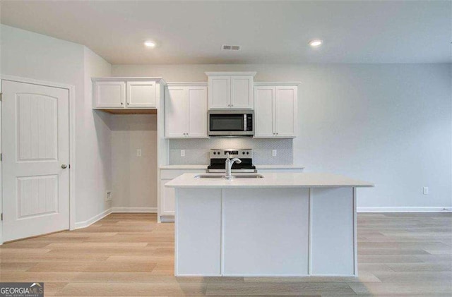 kitchen featuring white cabinetry, stainless steel appliances, tasteful backsplash, sink, and a kitchen island with sink