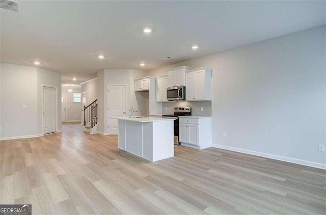 kitchen with a kitchen island with sink, light hardwood / wood-style flooring, white cabinetry, and appliances with stainless steel finishes