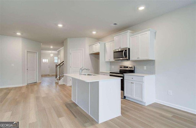 kitchen with sink, white cabinetry, appliances with stainless steel finishes, and a center island with sink