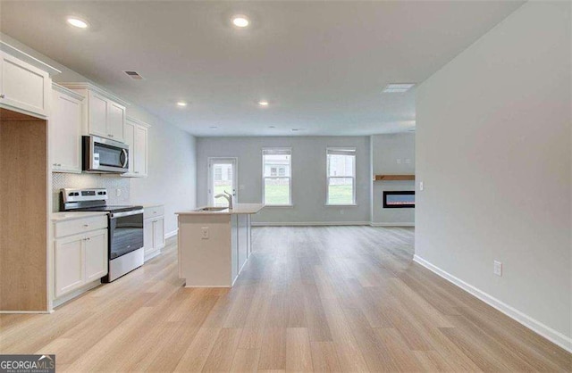 kitchen with white cabinetry, a kitchen island with sink, sink, backsplash, and stainless steel appliances