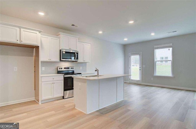 kitchen with appliances with stainless steel finishes, white cabinets, light wood-type flooring, sink, and an island with sink