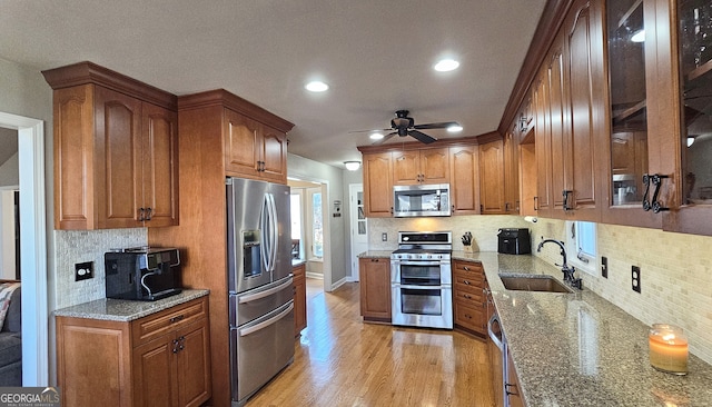 kitchen with appliances with stainless steel finishes, light stone countertops, sink, and light wood-type flooring