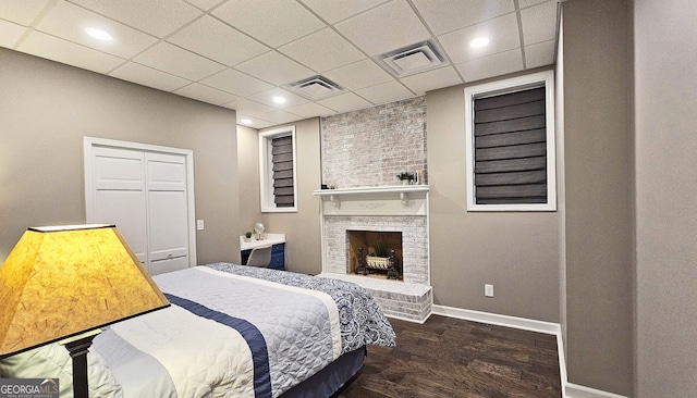 bedroom featuring a drop ceiling, a fireplace, and dark hardwood / wood-style flooring