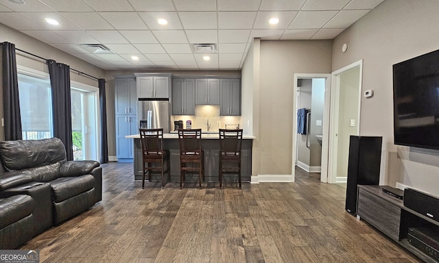 kitchen featuring dark wood-type flooring, a breakfast bar, gray cabinetry, a drop ceiling, and stainless steel fridge with ice dispenser