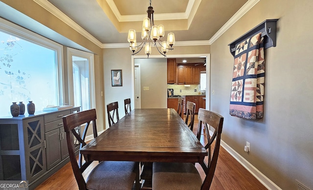 dining room featuring crown molding, dark wood-type flooring, a chandelier, and a tray ceiling