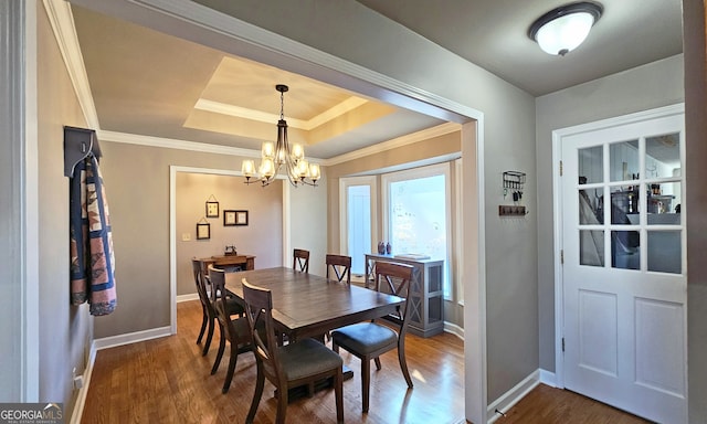 dining room with dark wood-type flooring, ornamental molding, a tray ceiling, and a notable chandelier