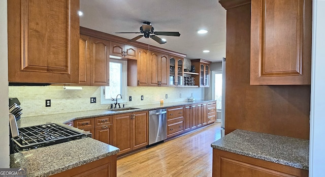 kitchen with sink, backsplash, stainless steel dishwasher, light stone counters, and light wood-type flooring