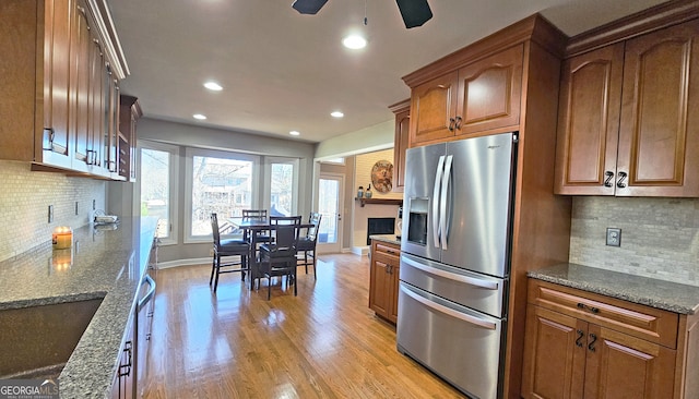 kitchen featuring decorative backsplash, dark stone counters, ceiling fan, stainless steel refrigerator with ice dispenser, and light wood-type flooring