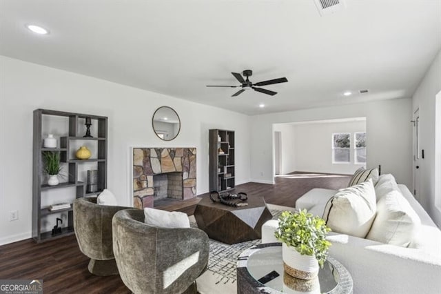 living room featuring a stone fireplace, dark wood-type flooring, and ceiling fan