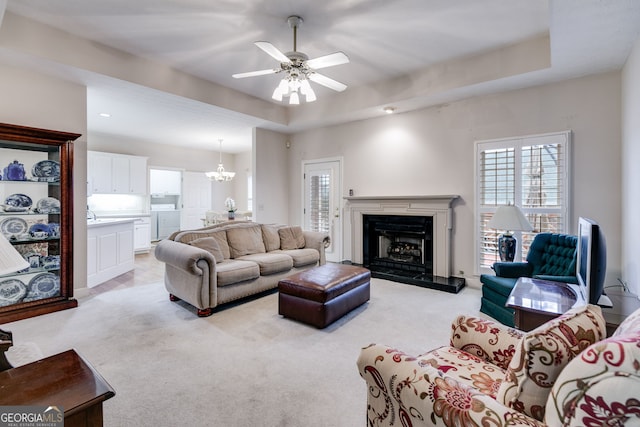 carpeted living room featuring ceiling fan with notable chandelier, a raised ceiling, and washer / clothes dryer